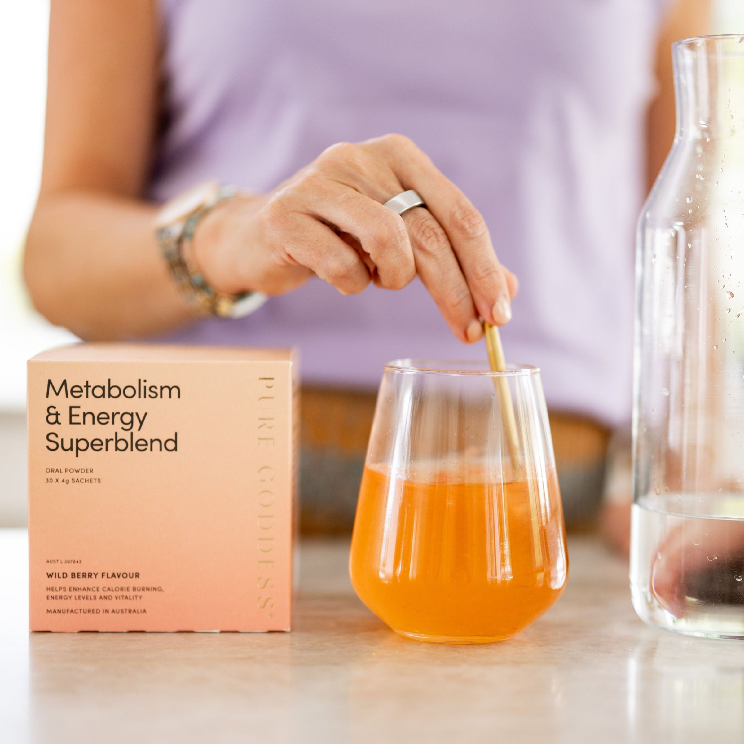 Person pouring a drink into a glass with a Metabolism & Energy Superblend box on a table.